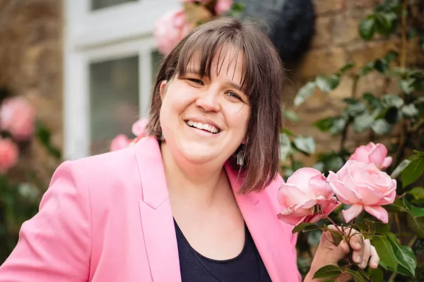 Steph wearing pink jacket standing in front of pink roses